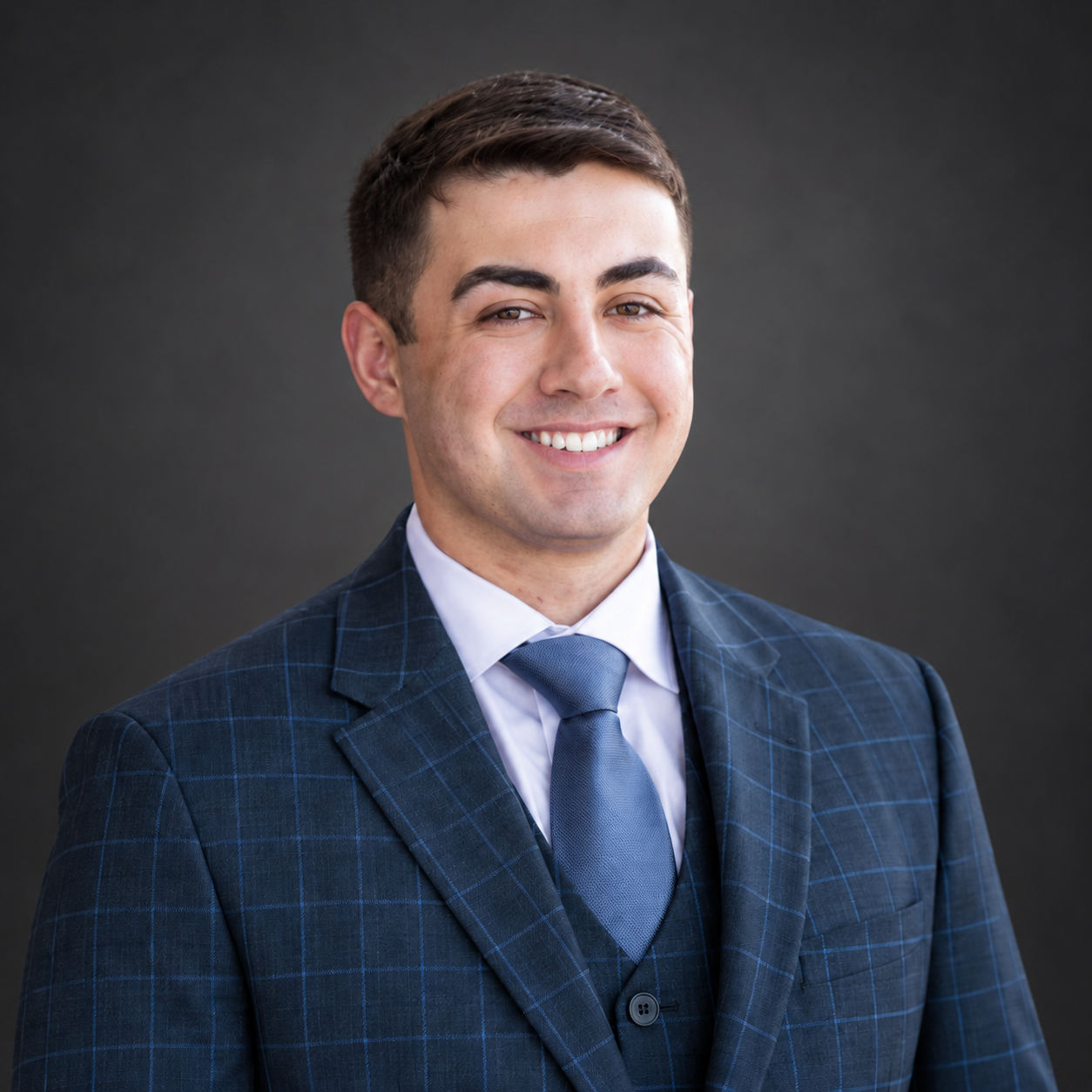 Cameron Chronister smiling in a navy suit against a charcoal background.