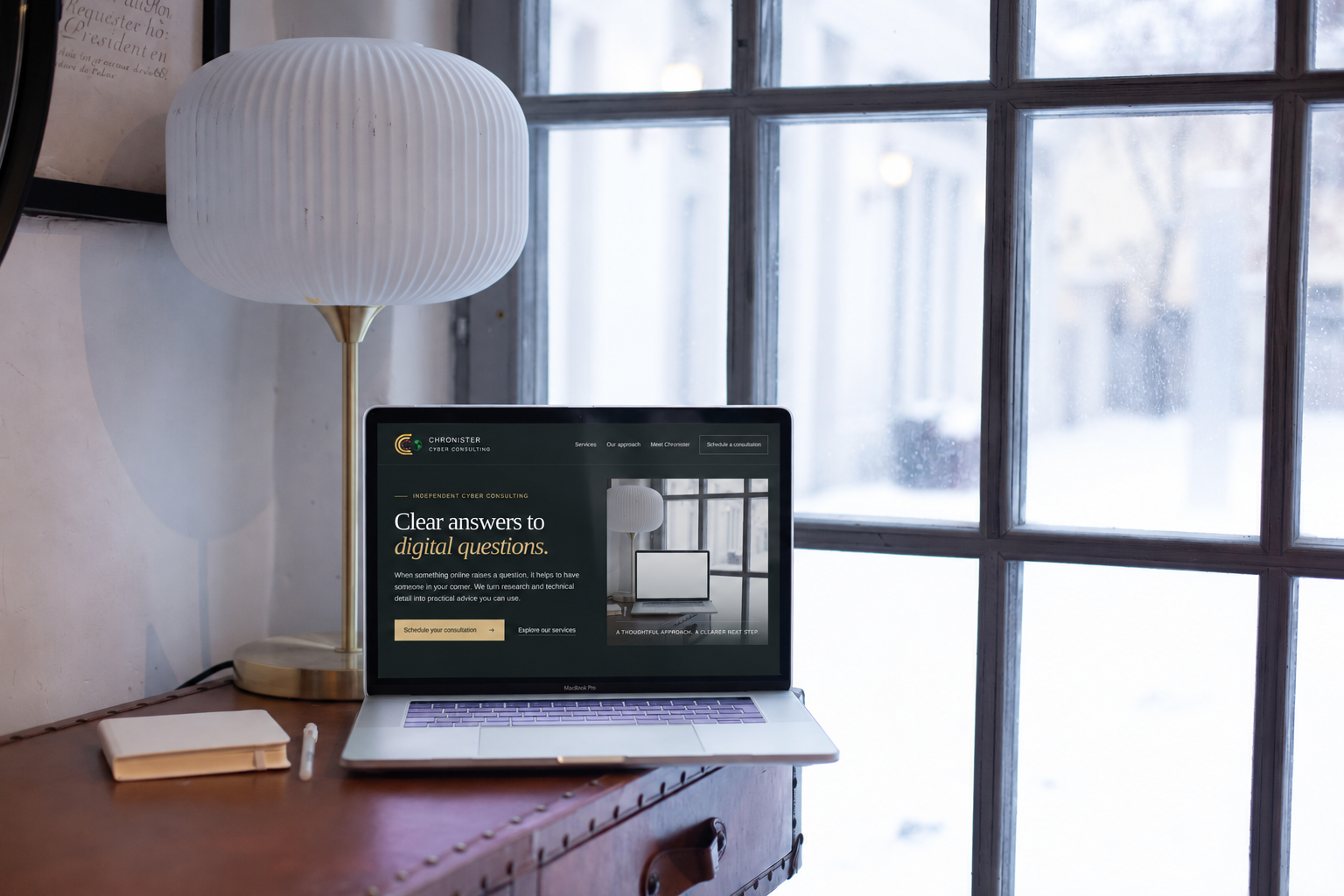 The Chronister Cyber Consulting homepage displayed on a laptop beside a notebook in a naturally lit workspace.